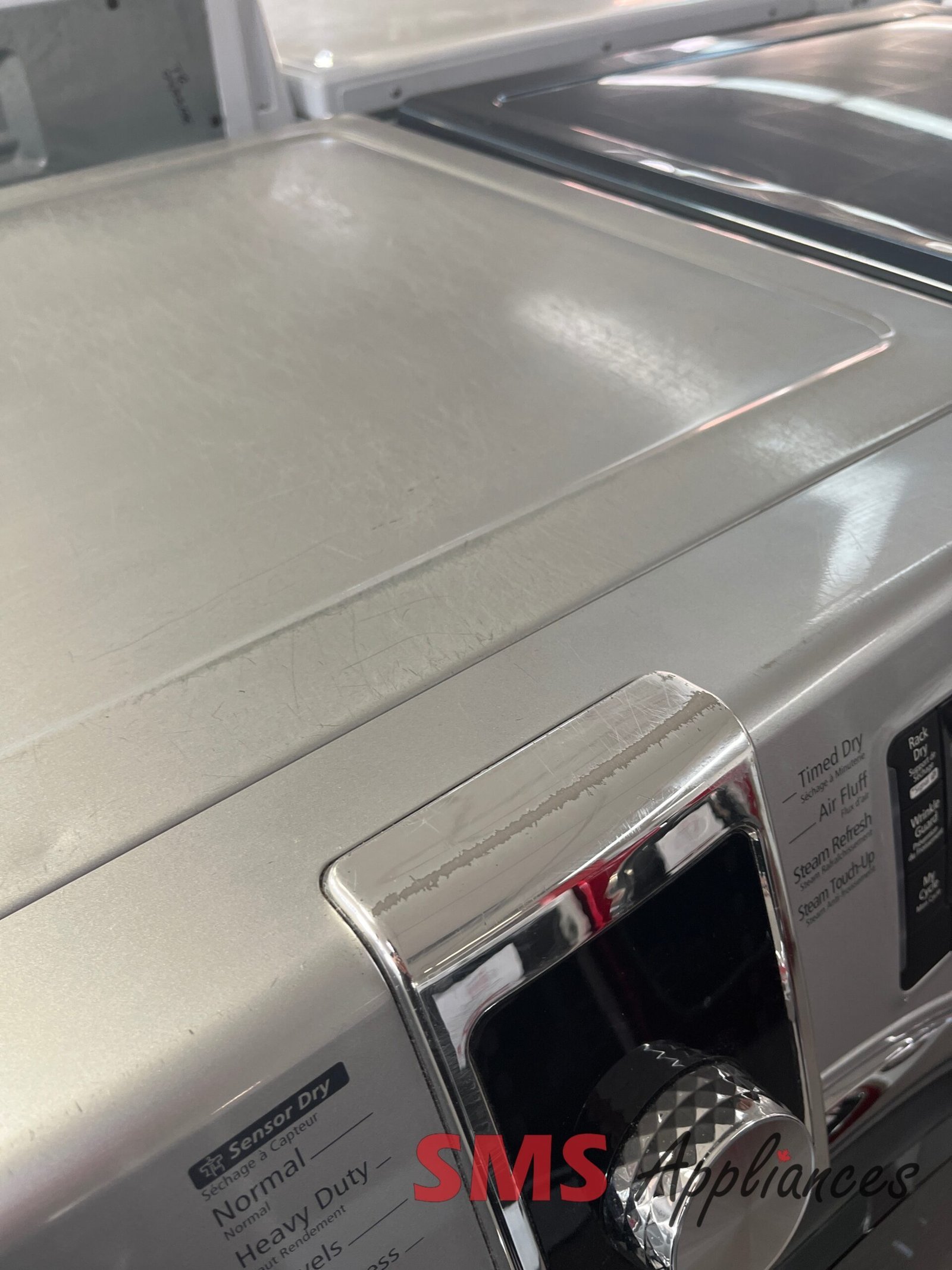Refurbished-Dryers-592-89457-6-scaled-1.jpg Silver front-loading washing machine with a rounded glass door and chrome trim, viewed from the side with a detergent panel visible at the bottom right.