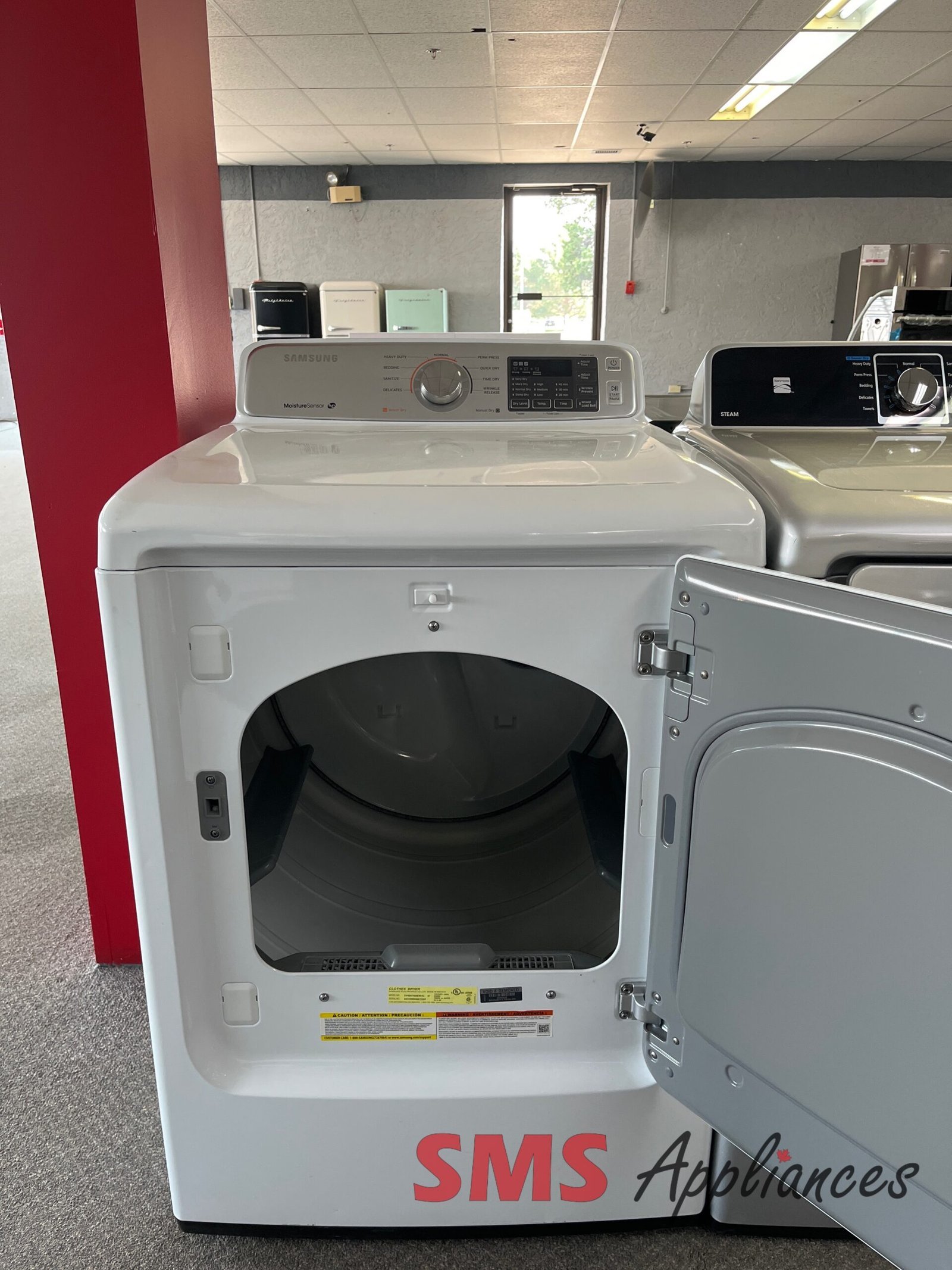 Refurbished-Dryers-DV45H7000EW-2-scaled-1.jpg Front-loading washing machines in a showroom, one door open, with control panel on top and SMS Appliances branding on the base edge