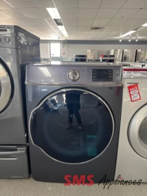 Front-loading Samsung washing machine on a showroom floor with other stainless appliances in the background and an 'SMS Appliances' sign at the base.
